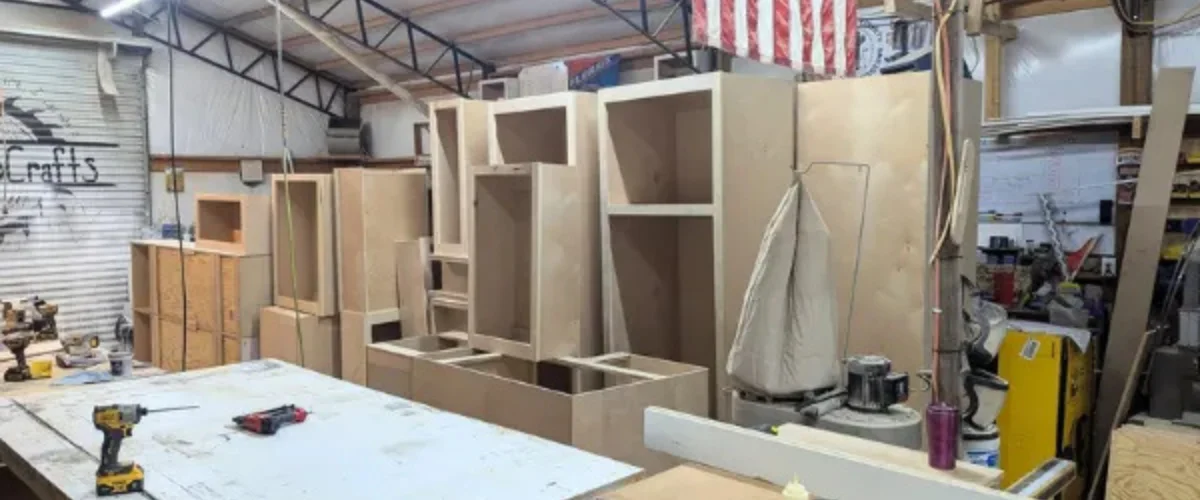 A wide shot of a woodworking shop filled with unfinished wooden cabinet frames and power tools on a workbench. A wide shot of a woodworking shop filled with unfinished wooden cabinet frames and power tools on a workbench.