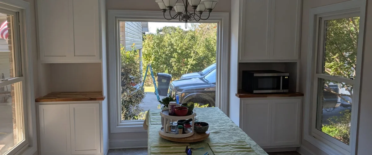 A kitchen dining nook with white built-in cabinets framing a large window looking out onto a lush garden. A kitchen dining nook with white built-in cabinets framing a large window looking out onto a lush garden.