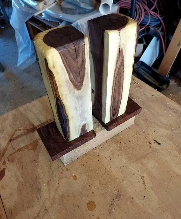 Two tall, rectangular block bookends made from wood with light and dark grain patterns, sitting on a wooden base.