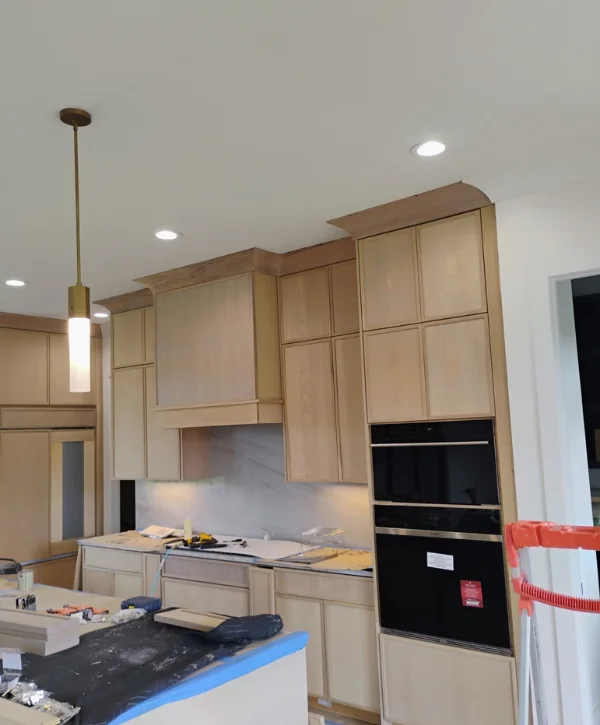 A newly installed kitchen with light wood cabinets, under-cabinet lighting, and modern black built-in appliances during construction.