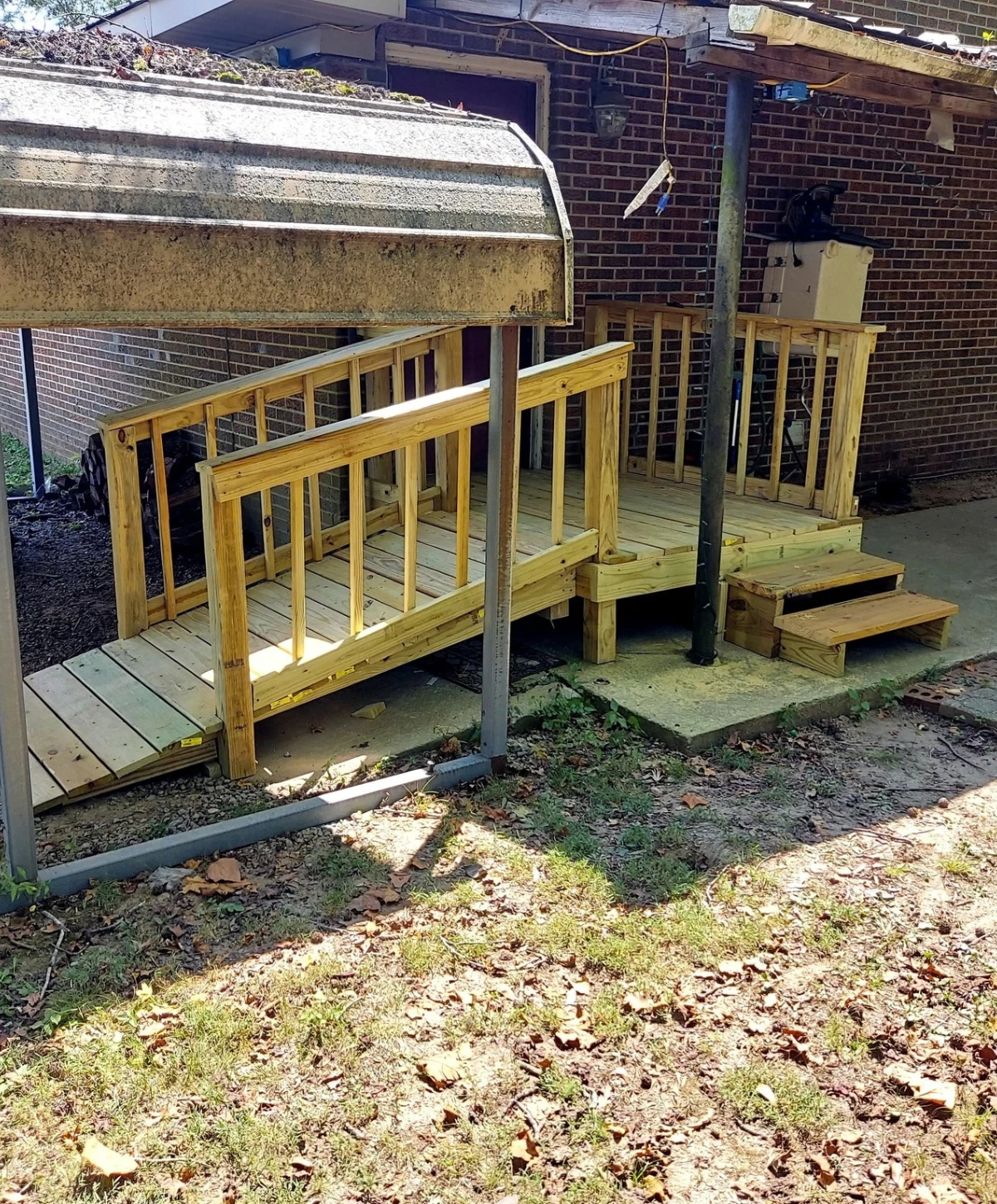 A newly built wooden accessibility ramp and steps leading to a brick house, partially covered by a metal carport.