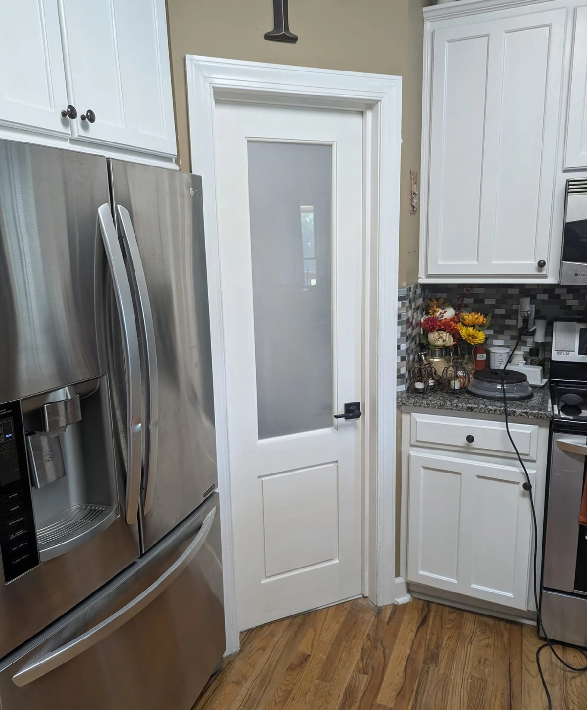 A kitchen interior featuring a stainless steel refrigerator next to a white pantry door with frosted glass.