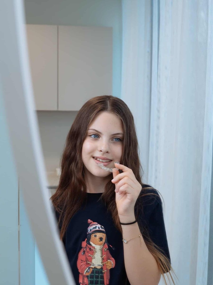 Tinejdžerica sama stavlja Invisalign aligner pred ogledalom