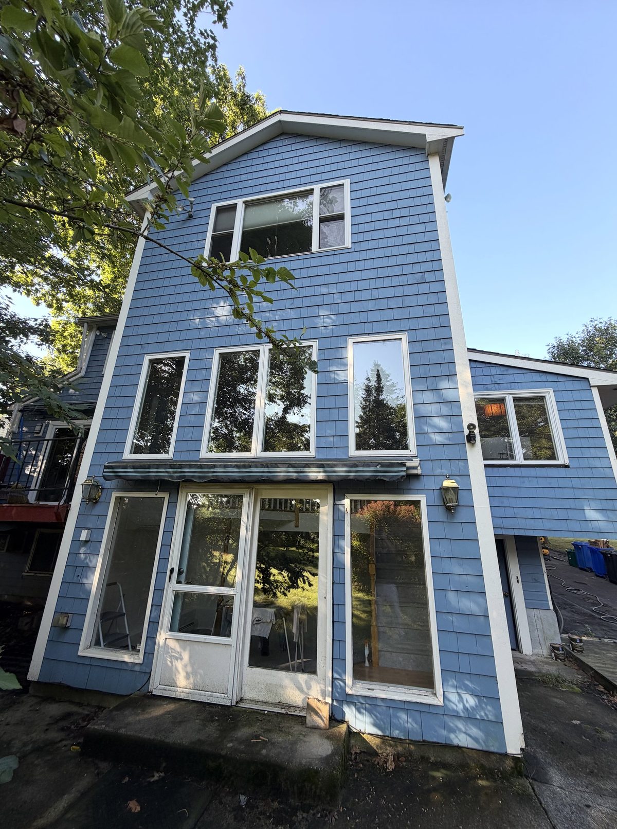 A three-storey house in washed-out medium blue with dulled trim and weathered shingle.