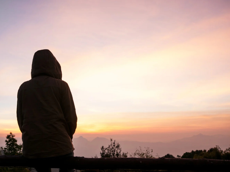 A person in a hood looking out at a sunrise