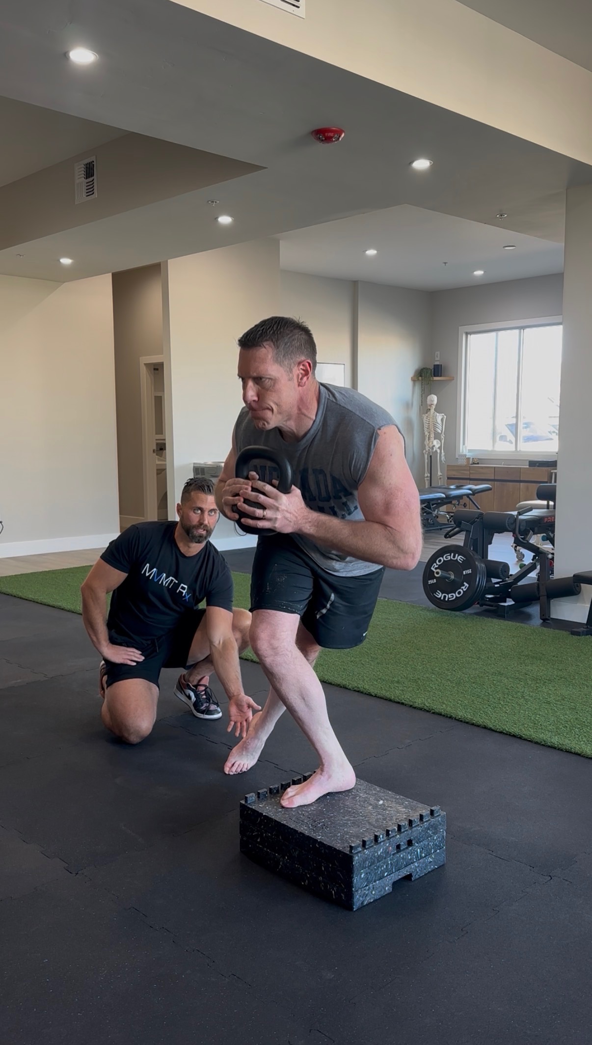 Cody Johnson performing a weighted step-up with kettlebell while Dr. Kyle Hemsley coaches at MVMT Rx in Sparks NV
