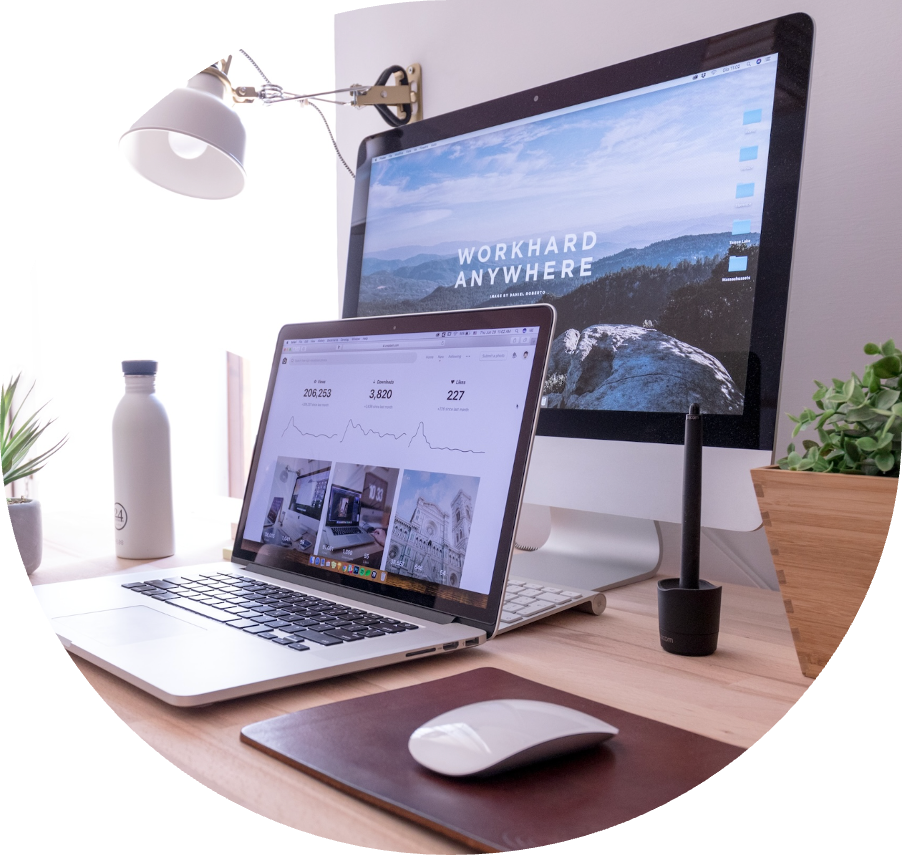 Laptop and desktop computer displaying productivity analytics and a scenic background, with a water bottle and plant on a wooden desk, illustrating a modern workspace for virtual assistant services.