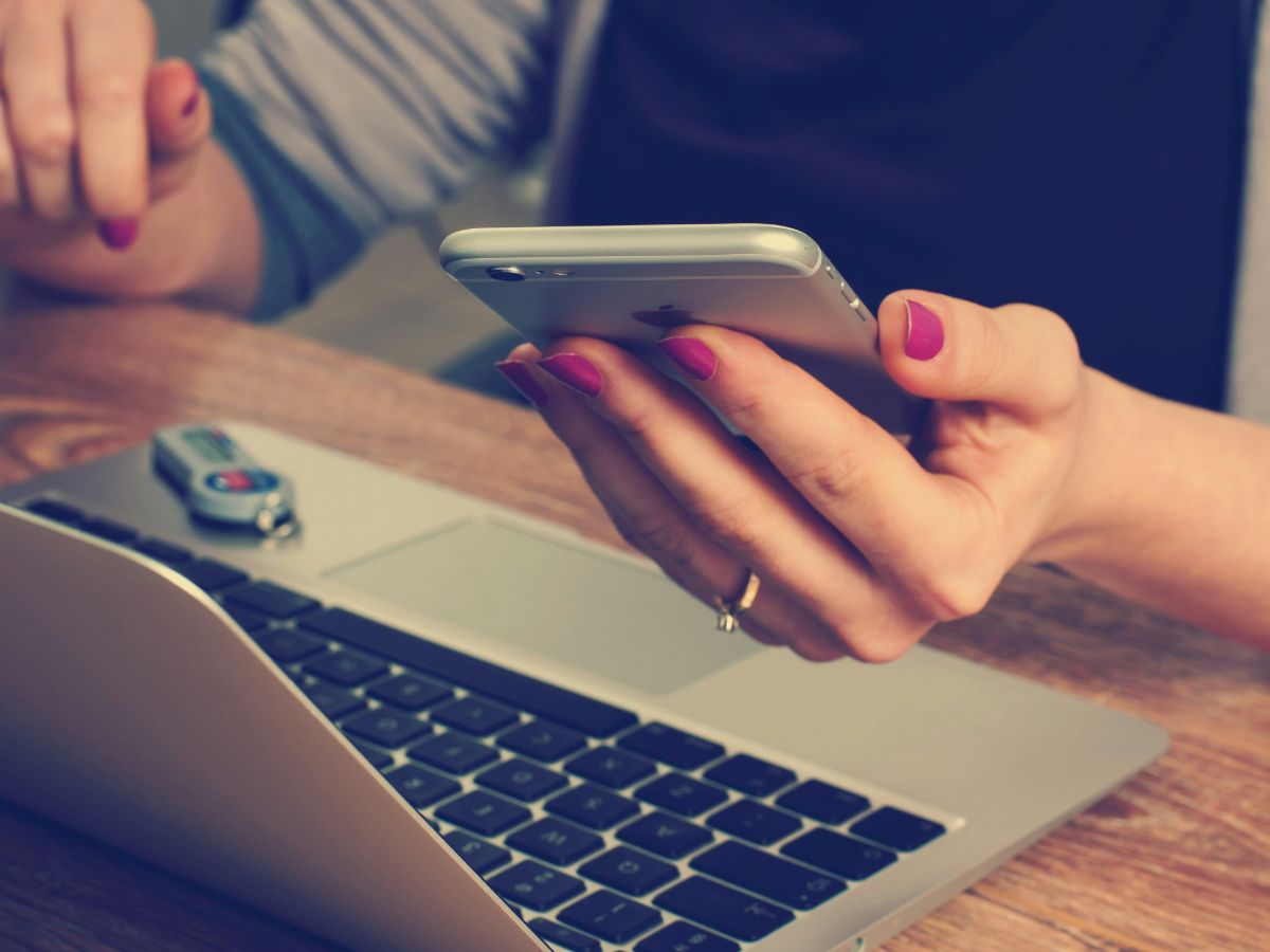 Person using smartphone while working on laptop, illustrating productivity and virtual assistant services for Every Task LLC.