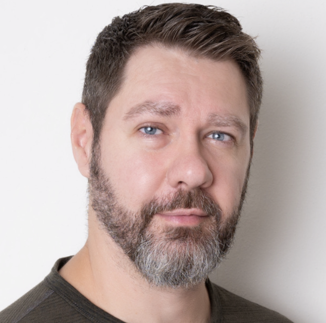 Bearded man with blue eyes and short hair, looking directly at the camera against a plain background, representing expertise in marketing and social media services.