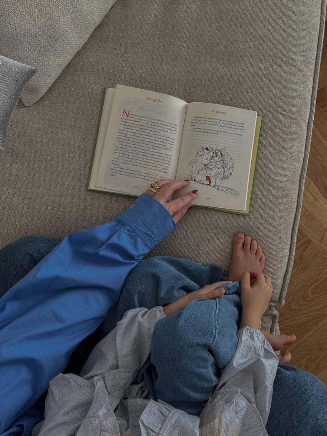 Parent and child sitting together on a bed reading an open book, enjoying a quiet and cozy moment. 