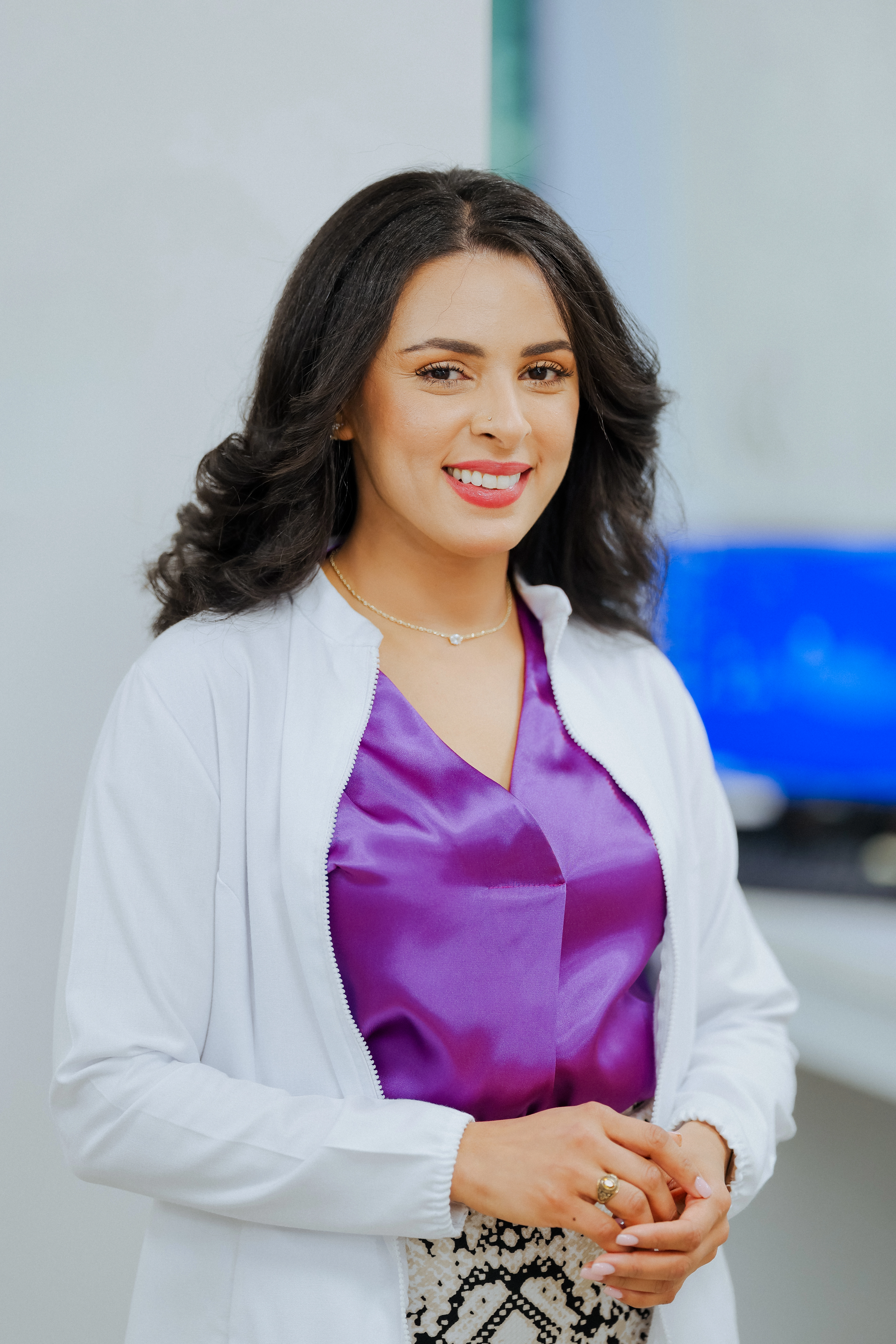 Portrait of a female dental professional wearing a white coat and purple scrubs in a modern dental office