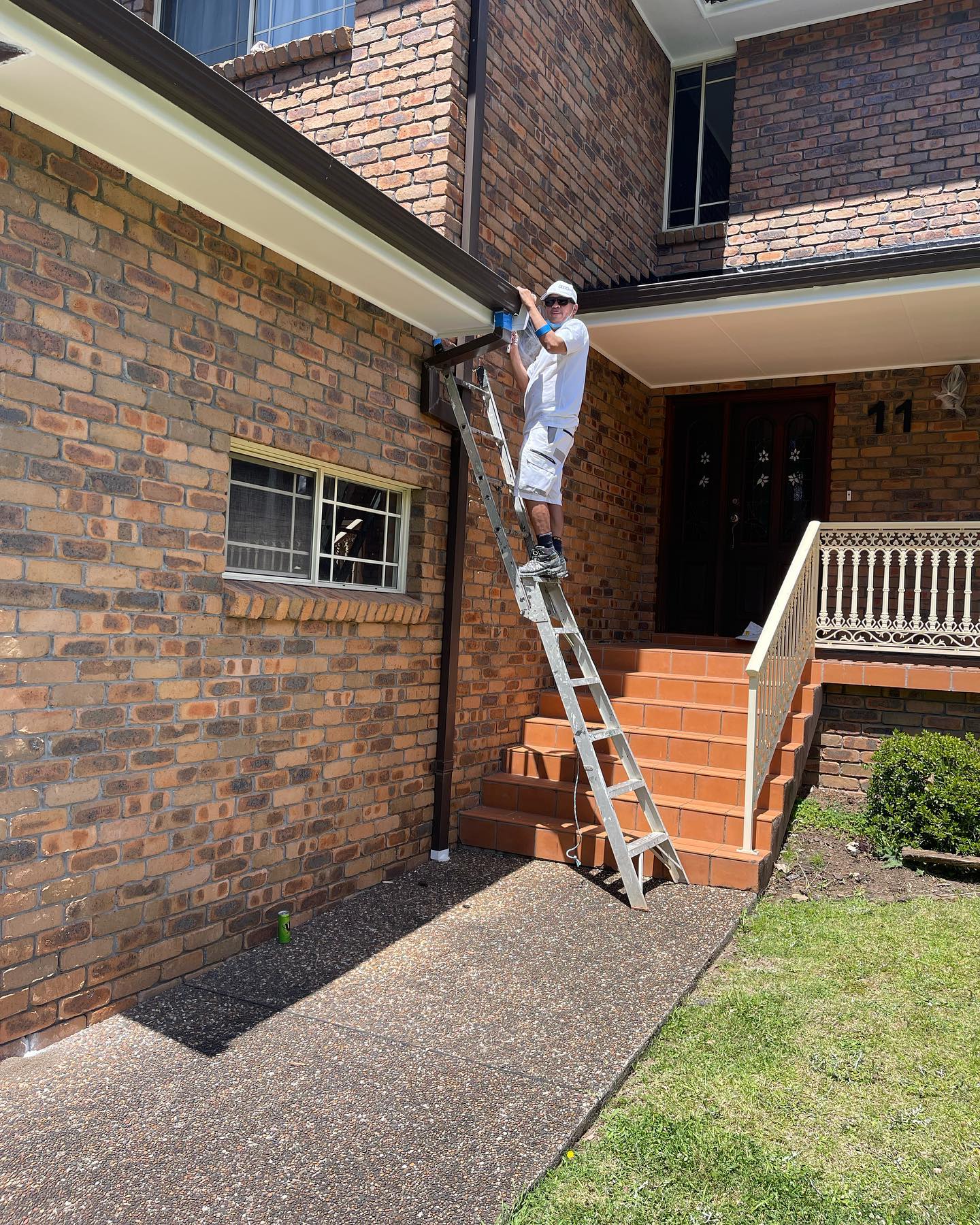 Painter on a ladder painting eaves on a brick home