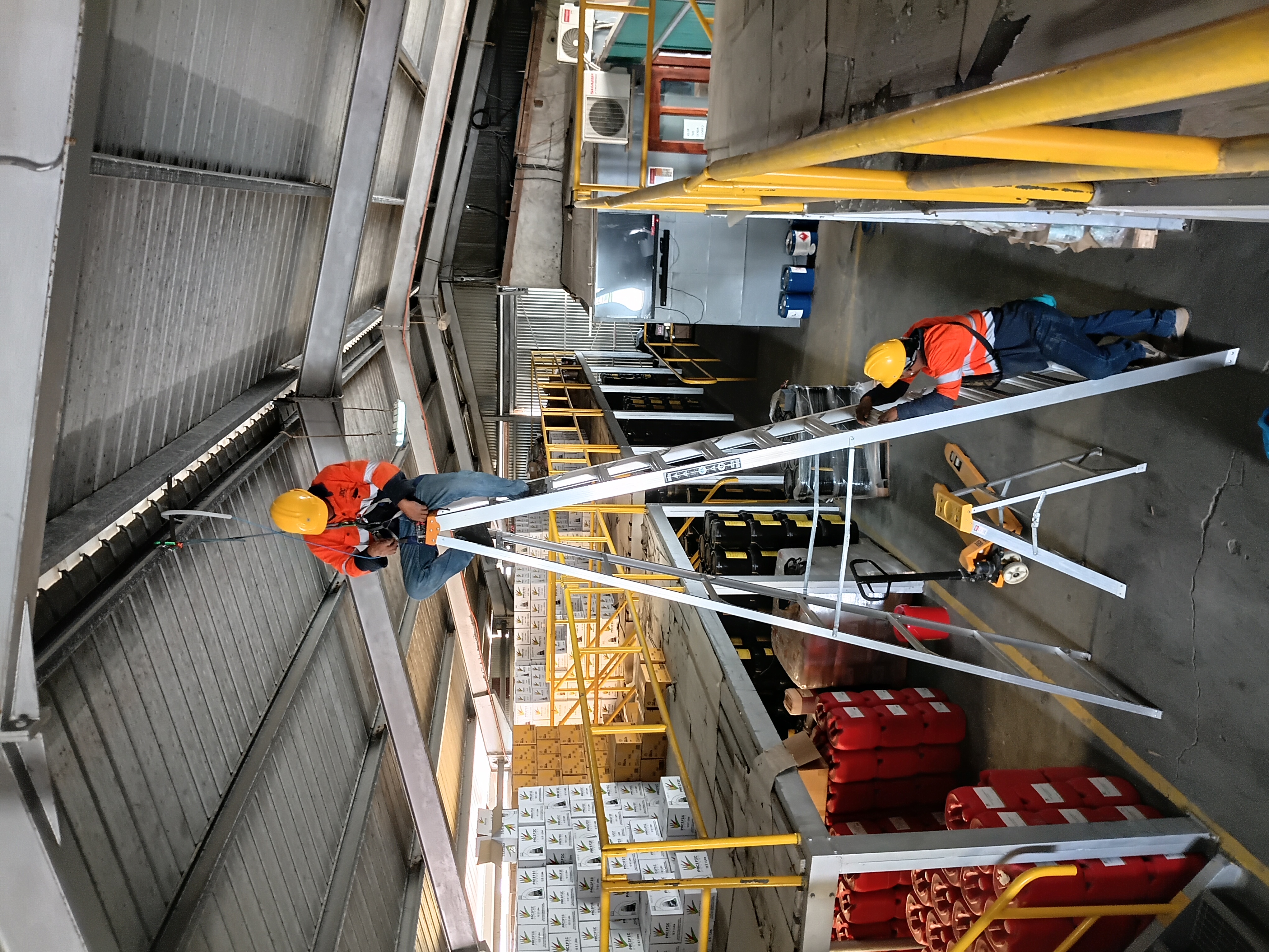 Two ODC technicians in high-visibility gear and hard hats running network cable along the roof steel of a warehouse in Port Vila, Vanuatu