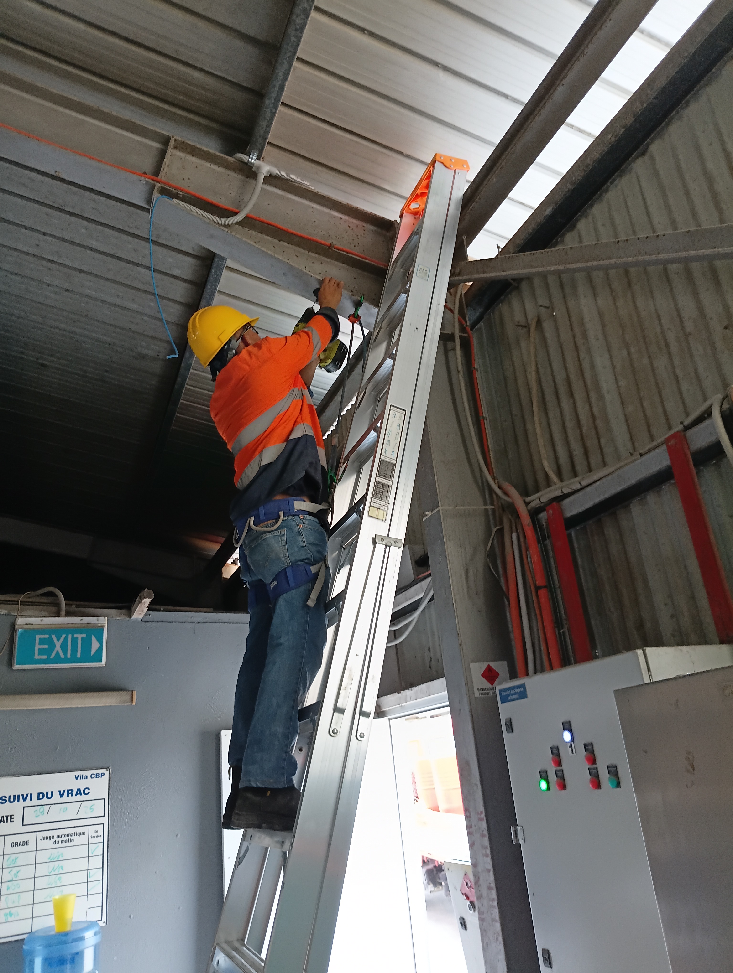 ODC technician on an extension ladder installing cable conduit at height inside a French-speaking industrial site in Vanuatu