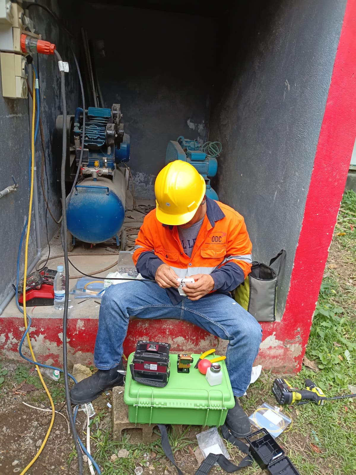 ODC fibre technician fusion splicing optical fibre on site at a pump house in Vanuatu, splicing kit open beside him
