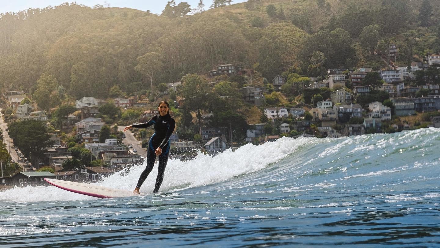 Zoe surfing a wave along a tree-lined coast