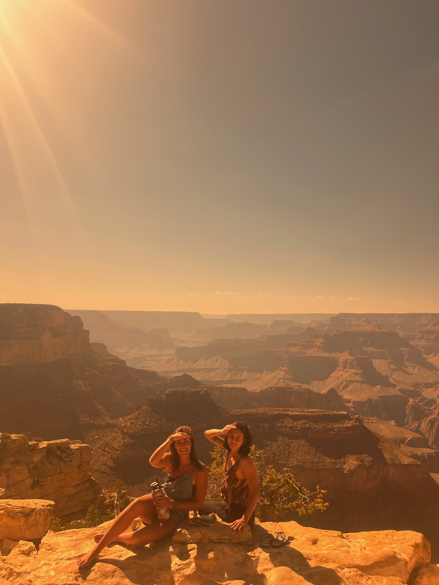 Two travelers sitting at a canyon rim at sunset