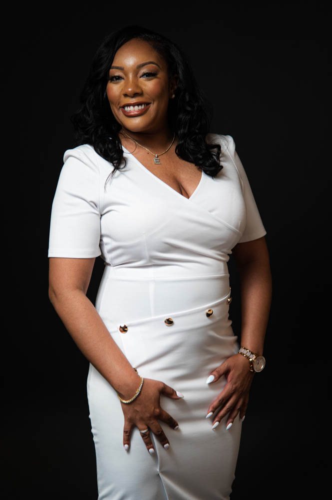 Dr. Eukeethia B. smiling in a white dress on a black backdrop