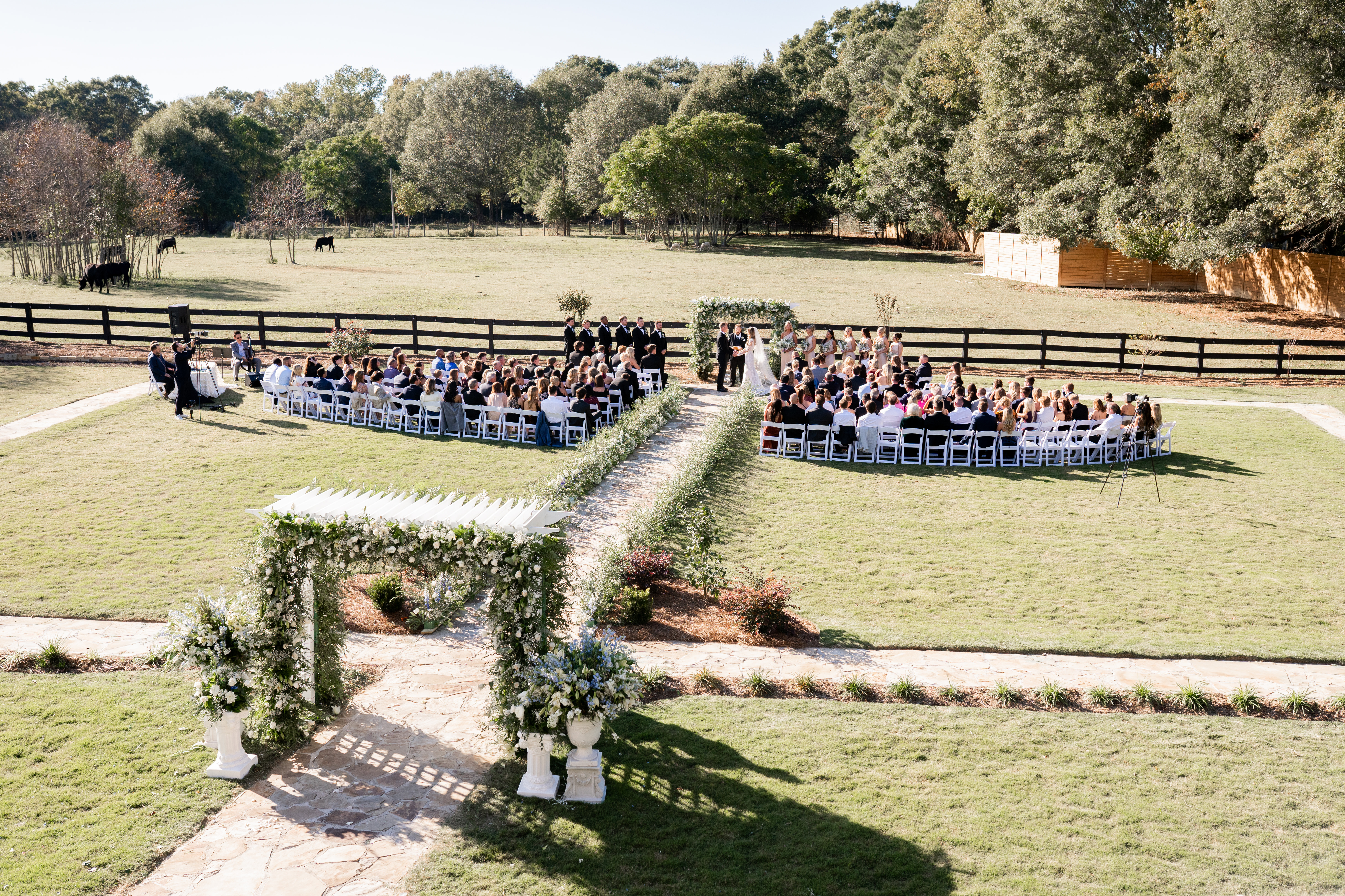 Outdoor wedding ceremony on the lawn at The Grove Estate, guests seated along a stone aisle facing a white floral arch
