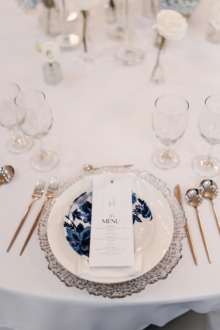 Elegant place setting with a glass charger, blue floral plate, gold flatware, and a printed menu card at The Grove Estate