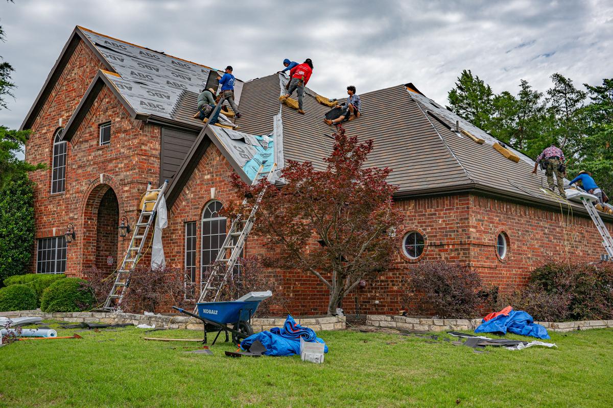 Roof tear-off underway on a brick home with crew clearing old shingles
