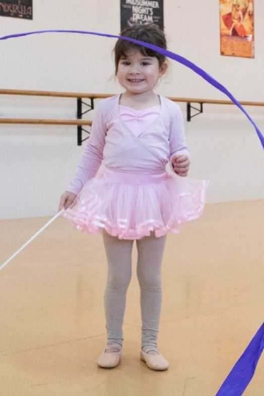A preschoolers uses a ribbon in ballet dance class in a tutu