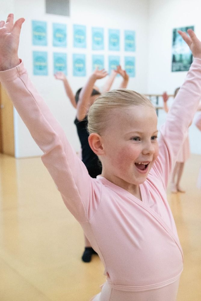An excited young dancer poses in ballet class