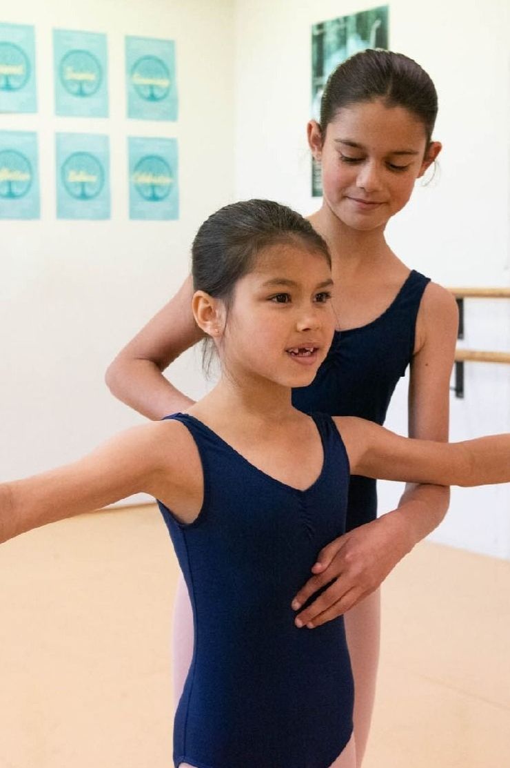 A dancer helps a younger dancer in ballet class