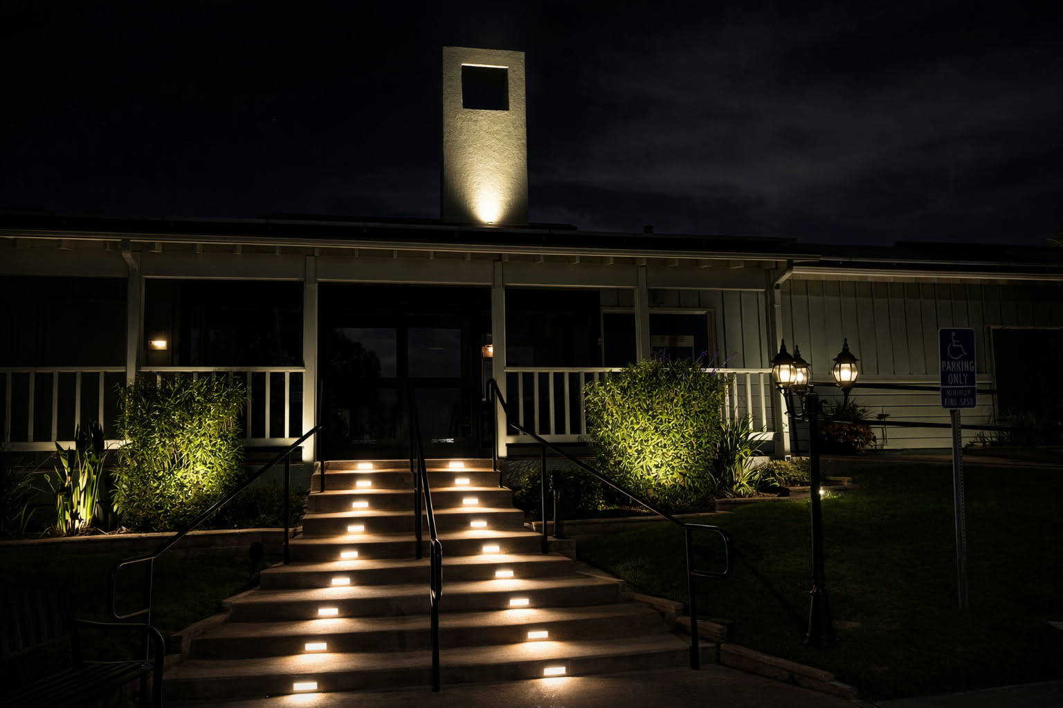 Warm stair lighting and softly illuminated shrubs at a building entrance