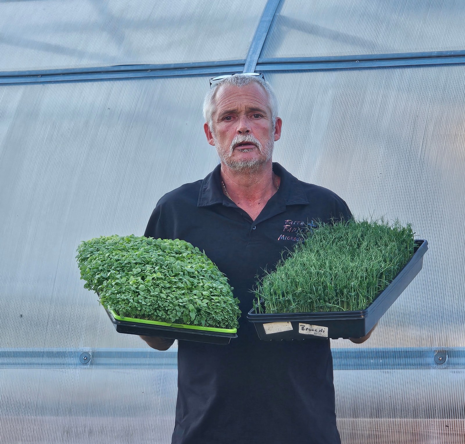 David Hall of North Florida Microgreens standing with two trays outside of the original grow tents in Ft. White, Fl.