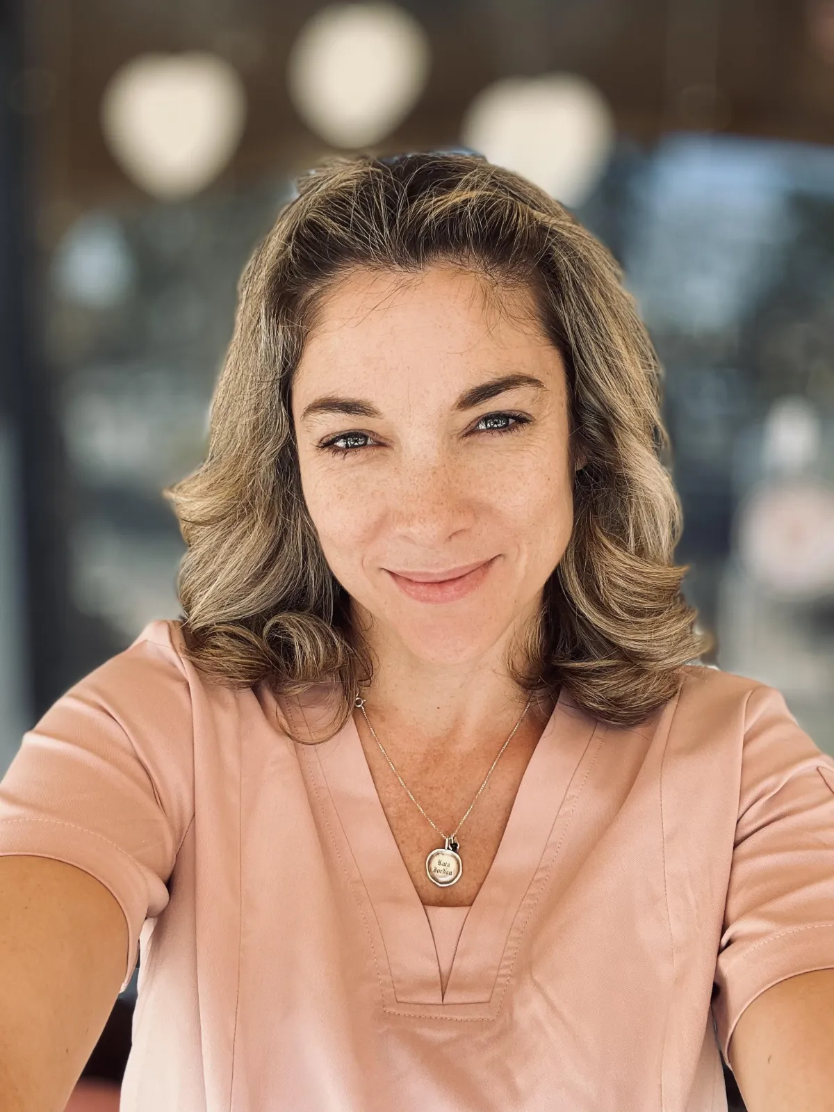 My friends a nurse founder, Colette, looking at the camera in her peach colored nursing scrubs