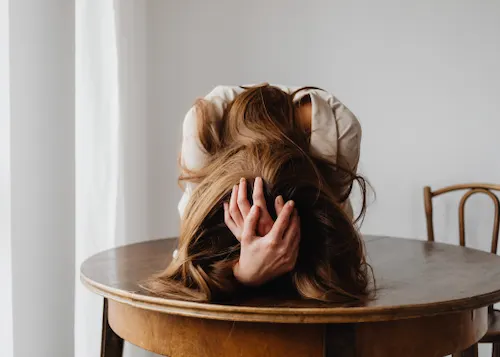 Woman with head down on a table, showing emotional overwhelm and grief after betrayal, representing women’s relationship coaching with Vanessa Cardenas.