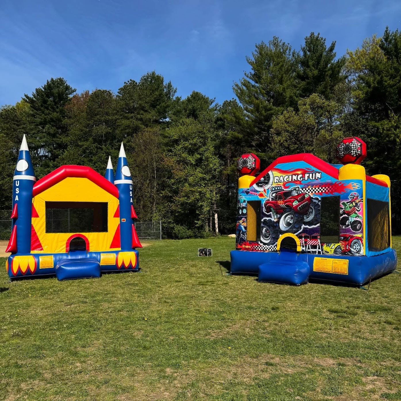 Two All Seasons Rent-All bounce houses, a rocket-themed unit and a racing-themed unit, set up on a Massachusetts lawn
