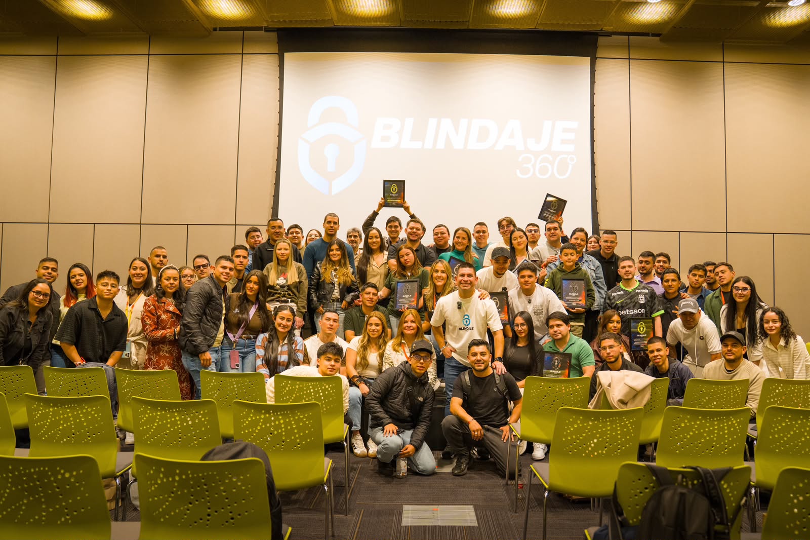 Alumnos de Blindaje 360 en un encuentro presencial, frente a la pantalla con el logo