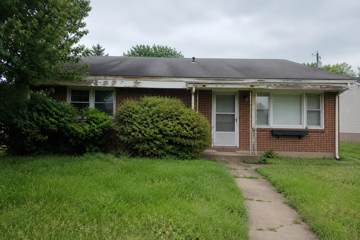 Brick rancher in as-is condition with overgrown landscaping and worn roof — the kind of home we buy
