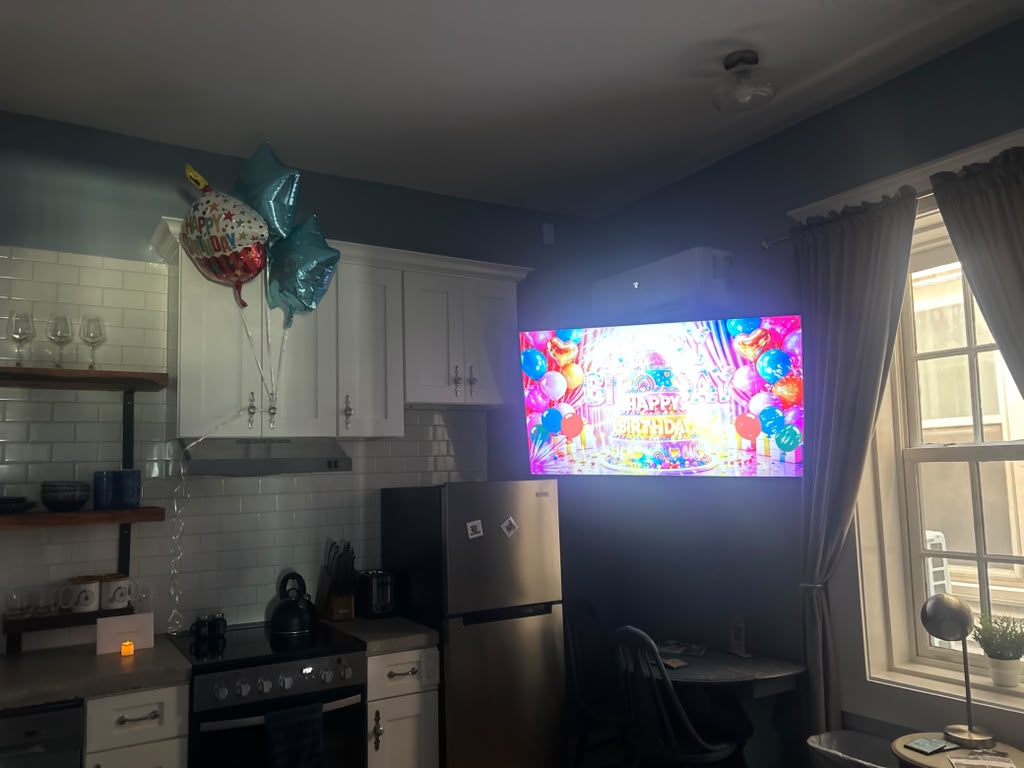 A suite kitchen with birthday balloons and a colorful birthday message on the TV