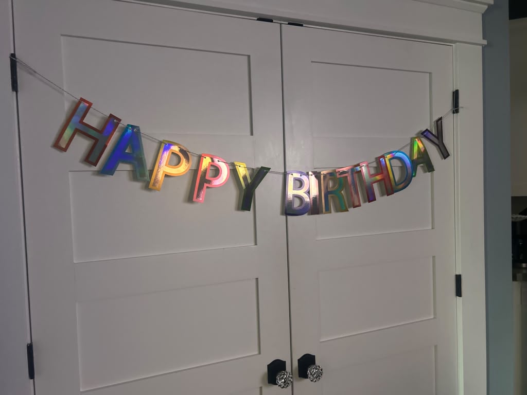 A holographic Happy Birthday banner hanging on white doors