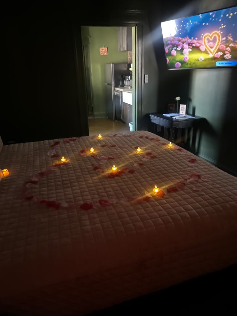 A candlelit suite with rose petals and a heart message on the TV