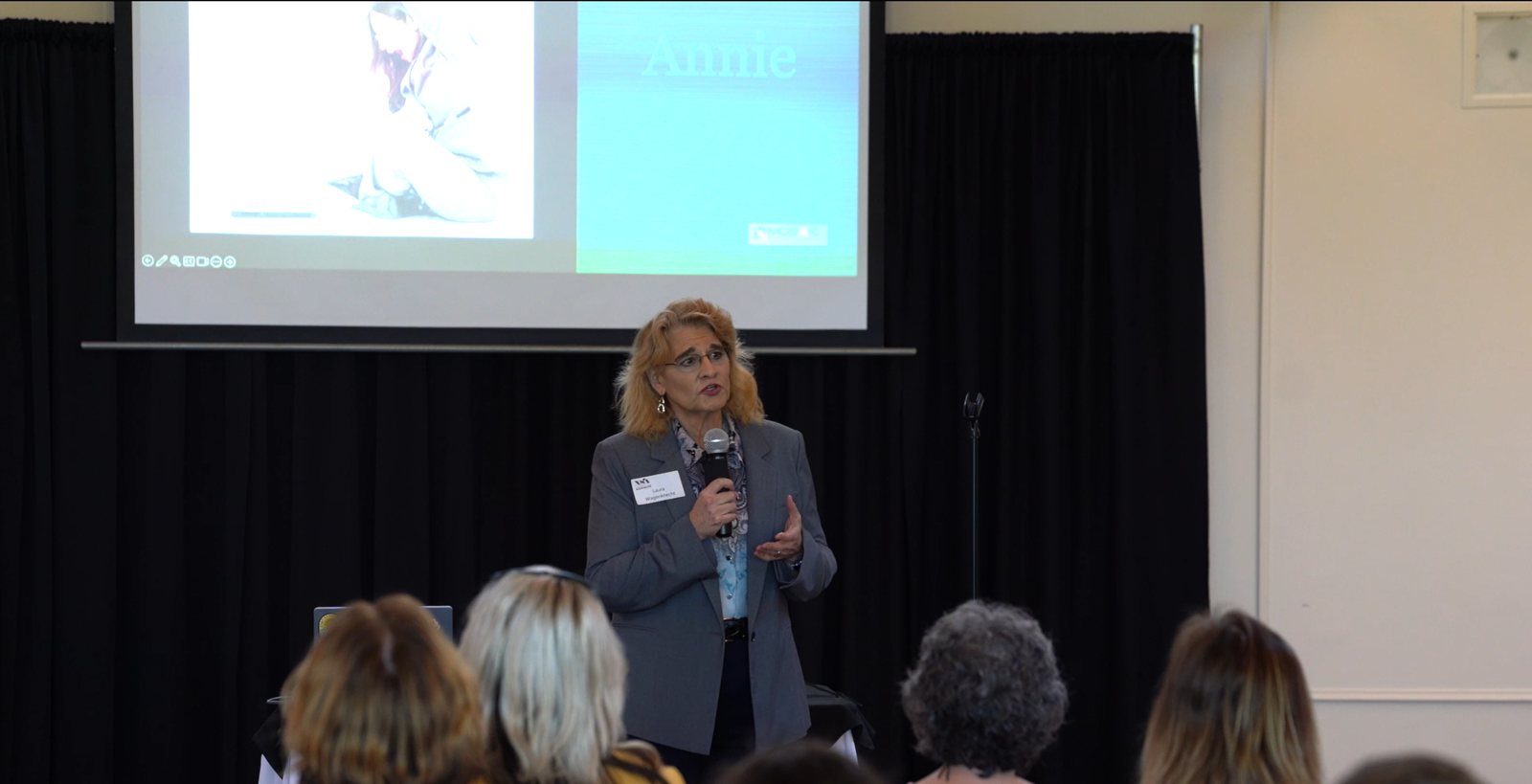 Laura Wagenknecht speaking to an audience with a microphone in front of a presentation screen