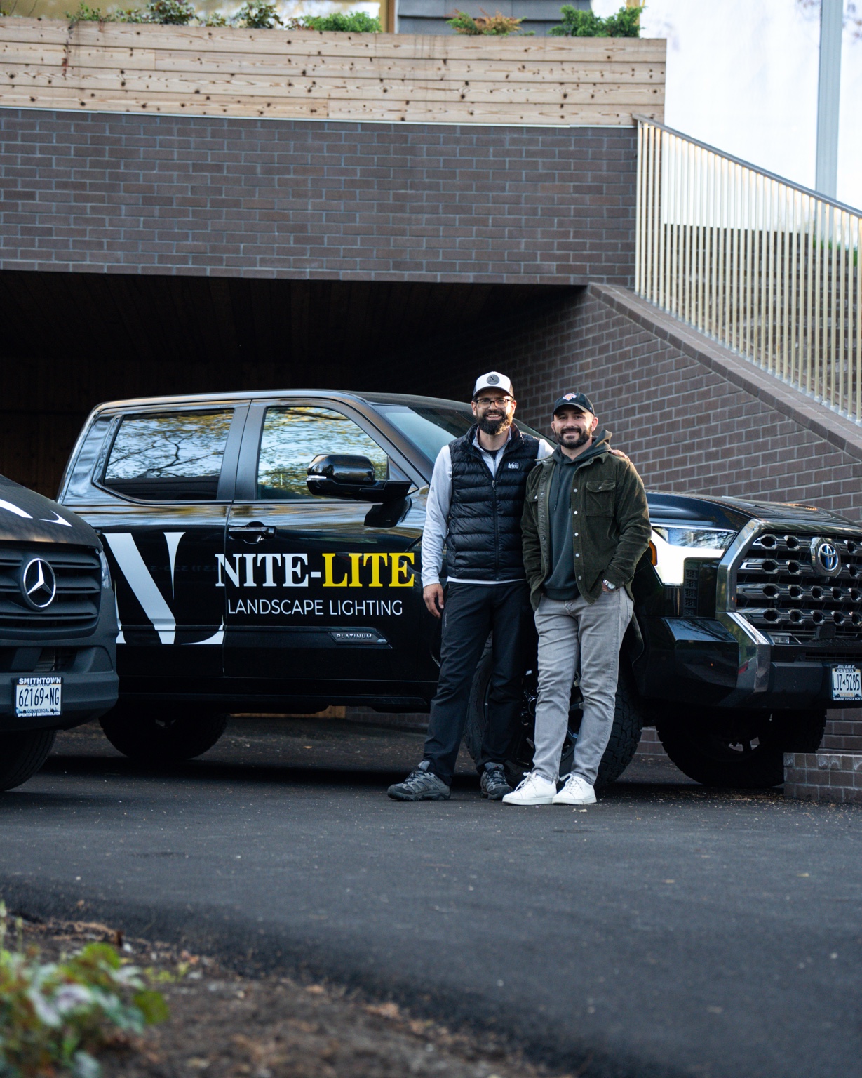 Two people standing beside a Nite-Lite Landscape Lighting truck
