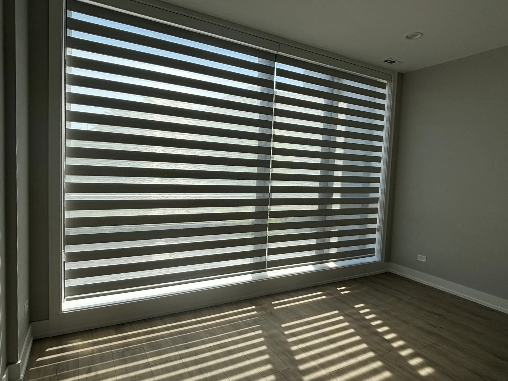 Large zebra shades casting soft striped light across a wood floor