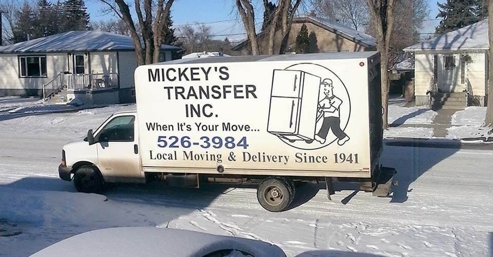 Mickey’s Transfer Inc white cube van with company name and phone number parked on a snowy residential street