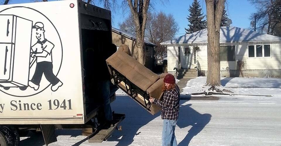 Mover lifting a tan armchair into the back of a Mickey’s Transfer Inc cube van on a sunny winter day