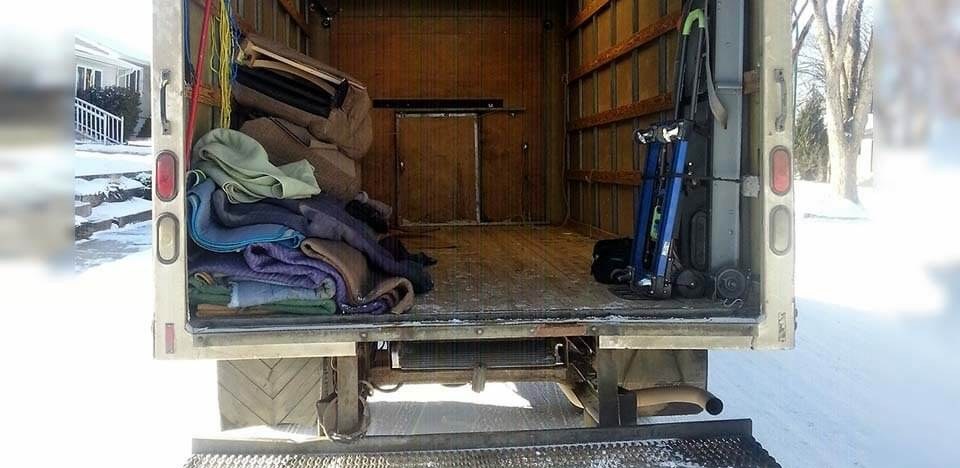 Inside a Mickey’s Transfer Inc cube van: stacked moving blankets and a hand truck on a wooden floor