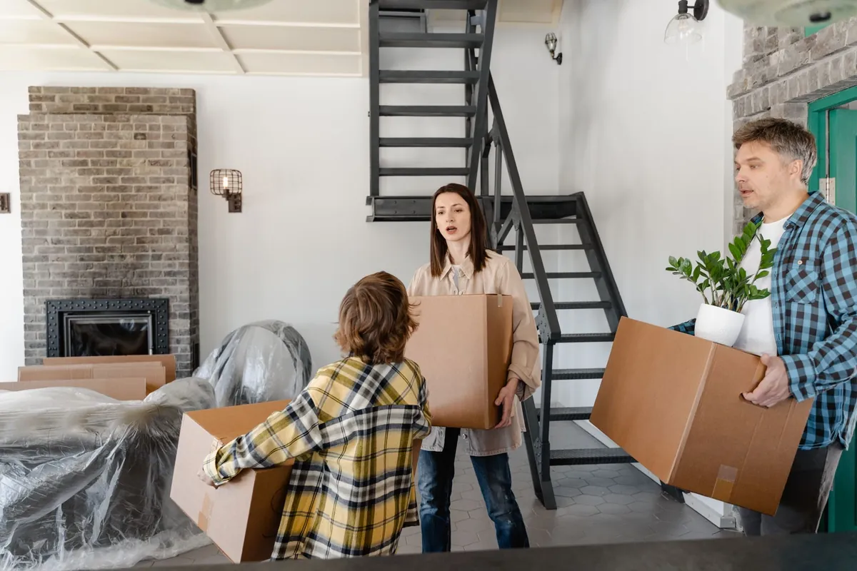 A family carrying boxes and a plant into a new home