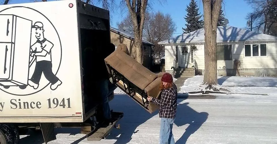 Mover lifting a tan armchair into the back of a Mickey’s Transfer Inc cube van on a sunny winter day