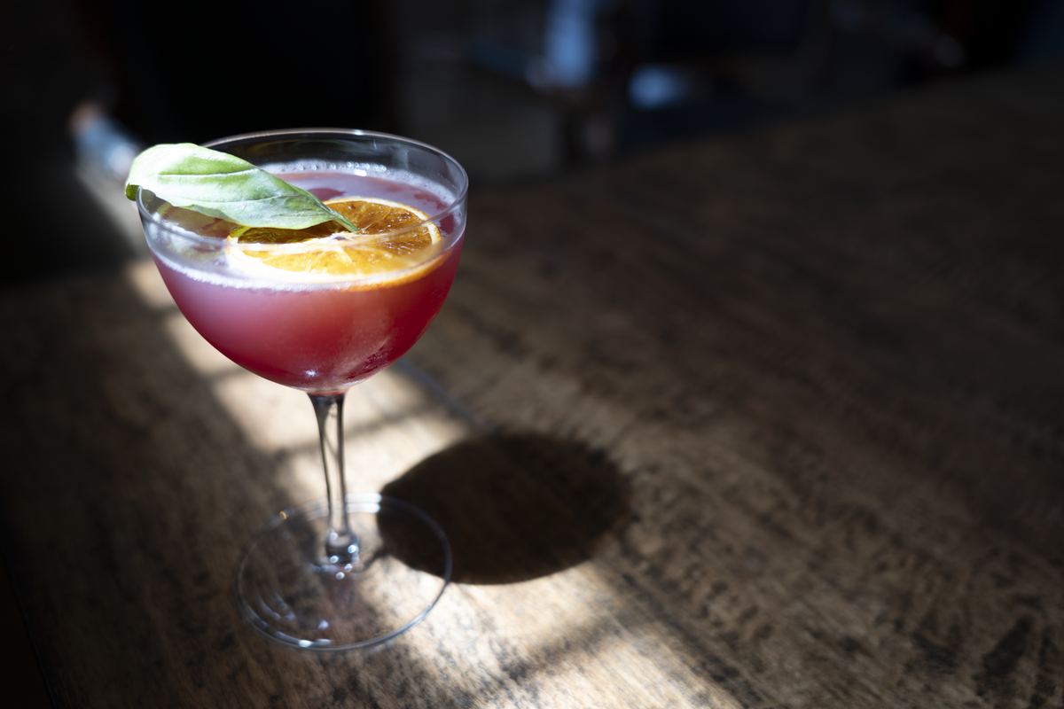Cocktail garnished with basil and dried orange in dramatic light