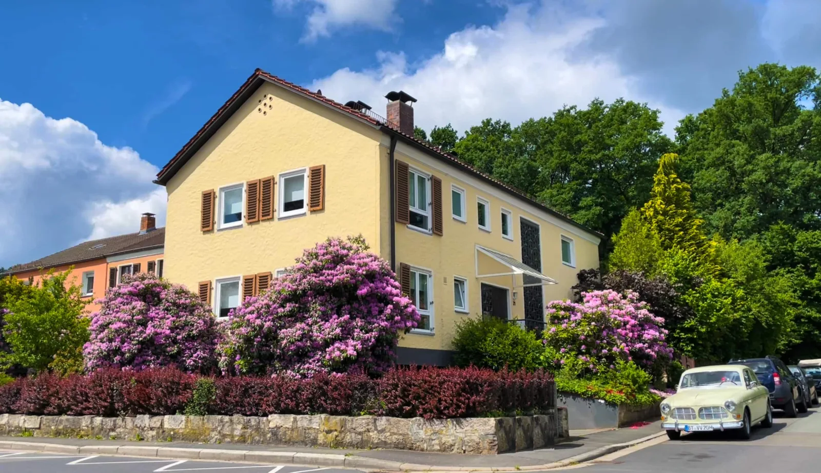 Das Apartmenthaus im Ahornweg 21 mit blühendem Rhododendron und Volvo-Oldtimer