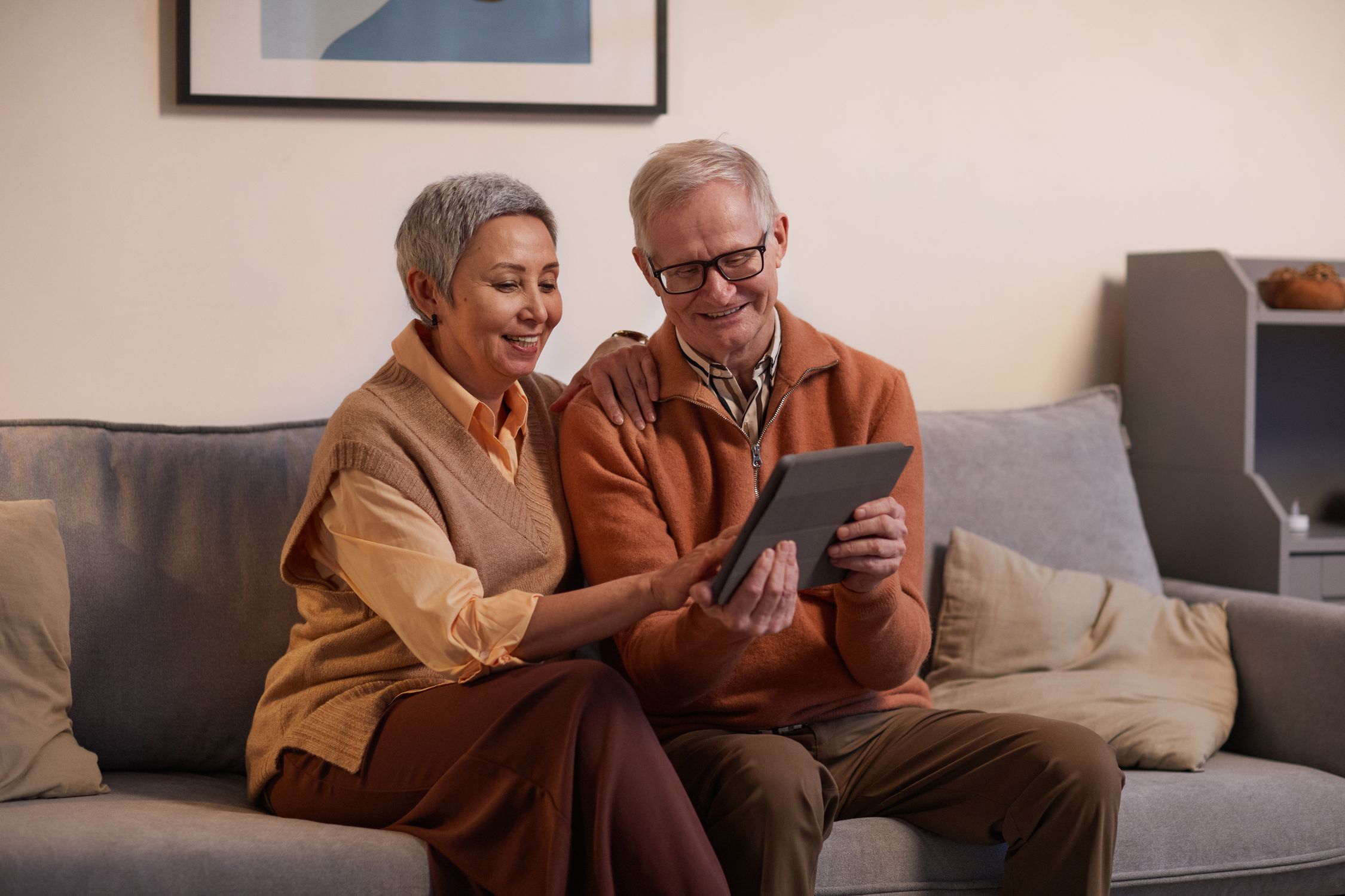 A smiling older couple browsing a tablet together in their living room
