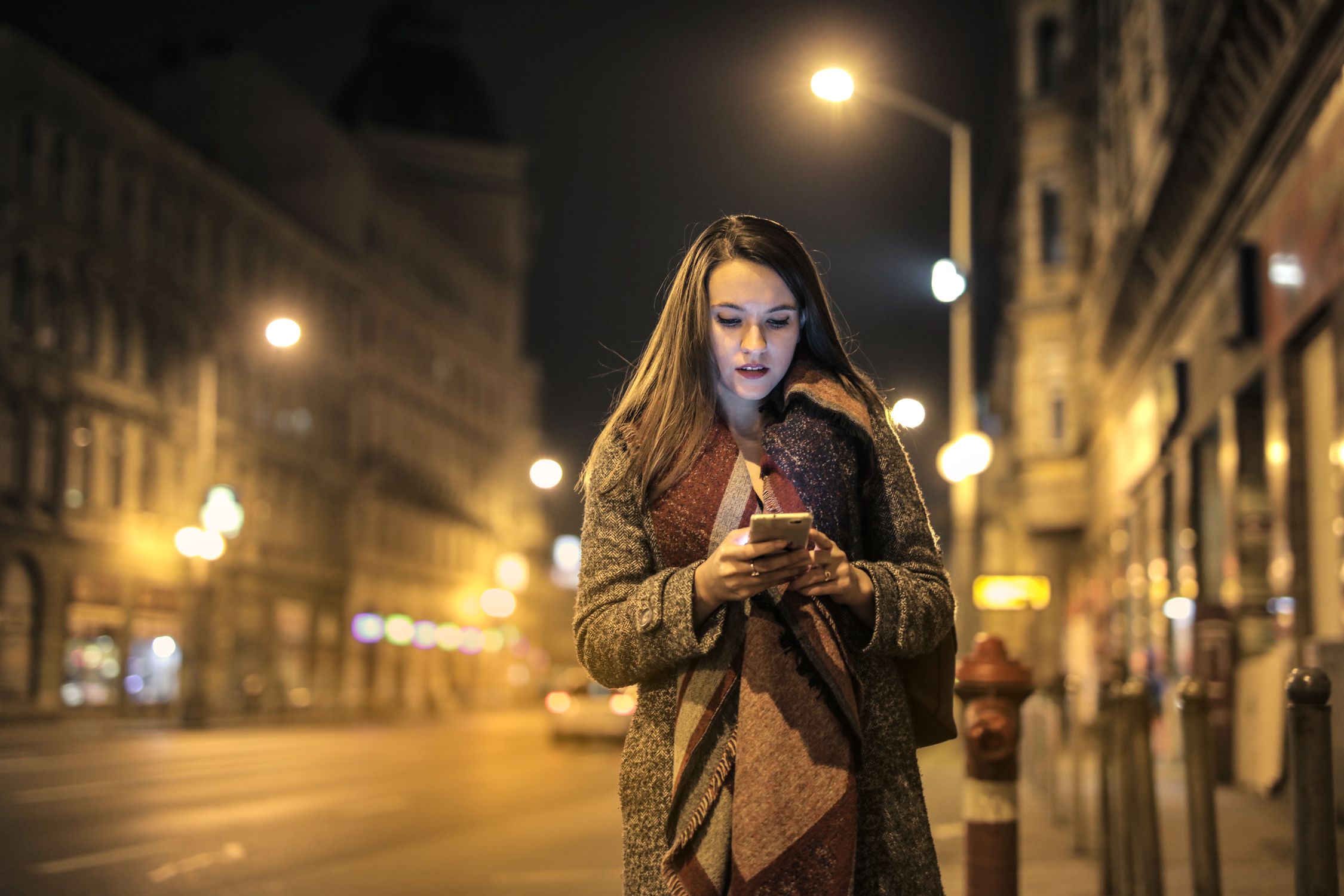 A woman checking her phone while walking along a city street
